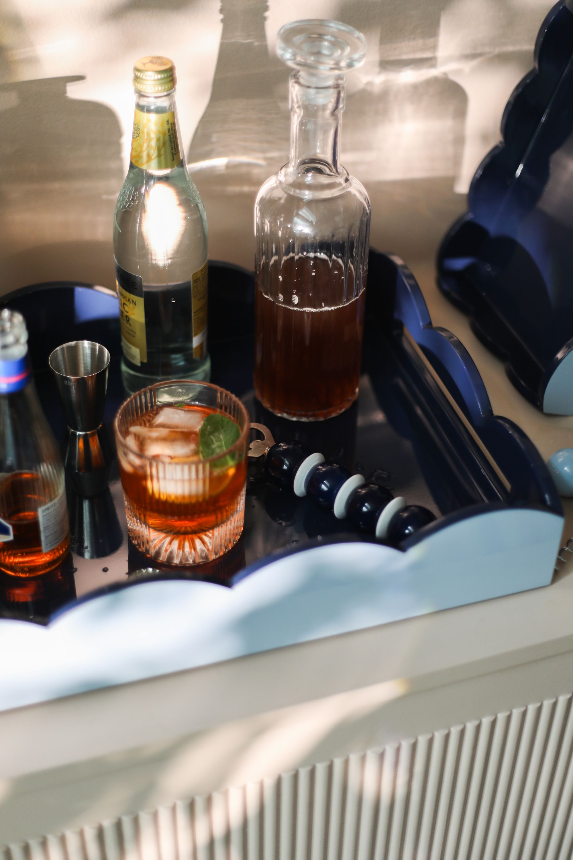 Image of a two-tone blue, scalloped tray with beverages in it on a white cabinet. 