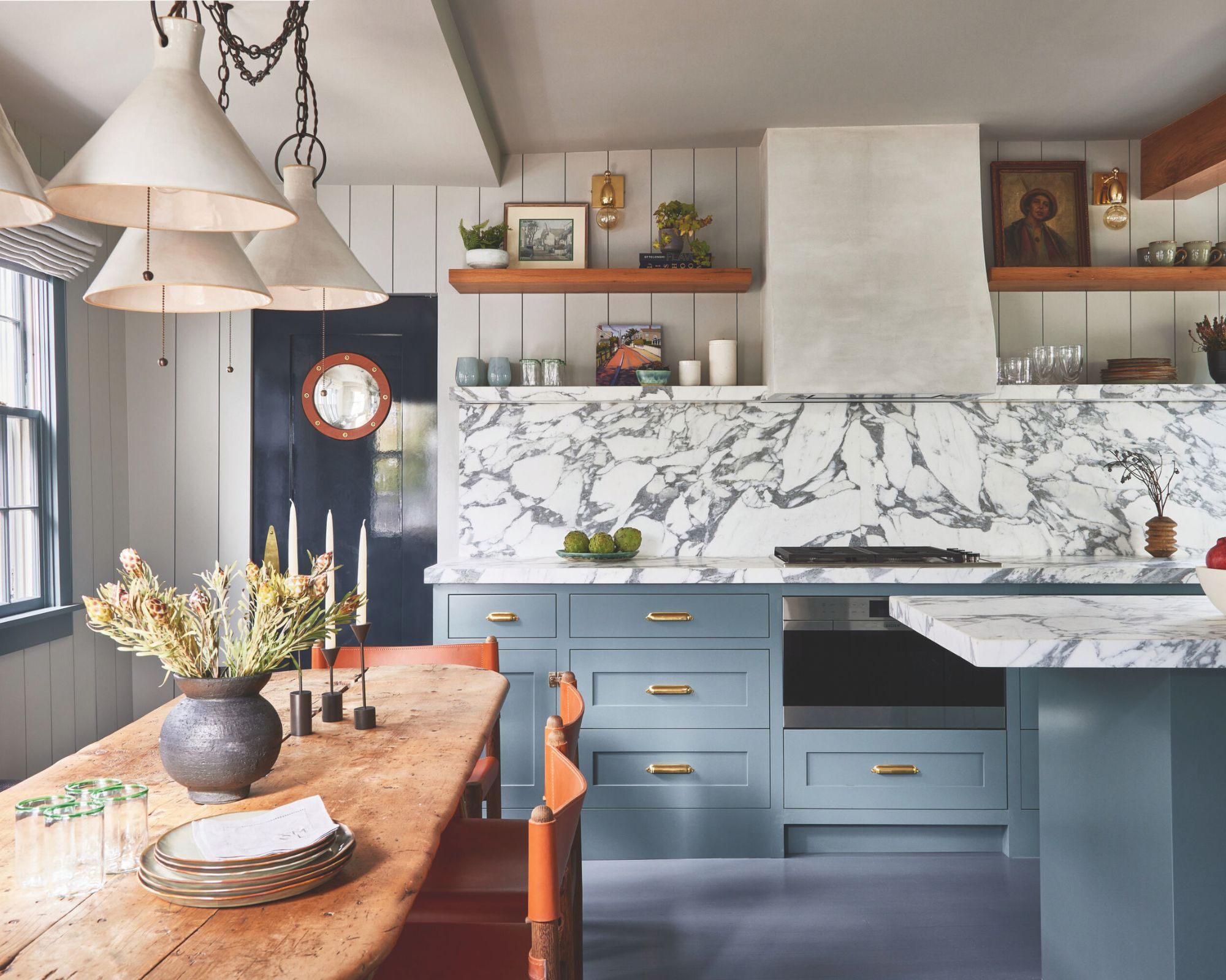 A modern rustic marbled kitchen with blue cupboards and a farmhouse kitchen table