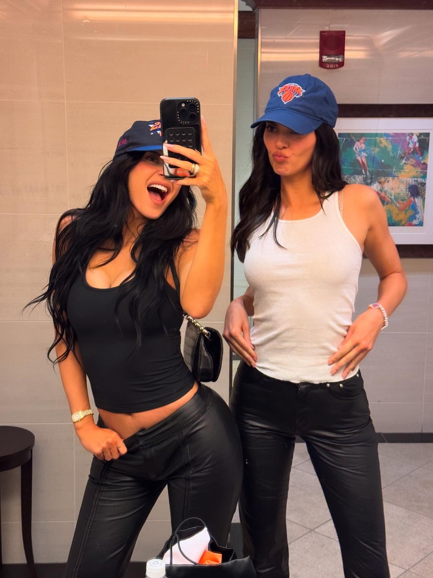 Kylie Jenner wears a black top and leather pants, and Kendall Jenner wears a Knicks hat, white Hanes tank top, and black leather pants.