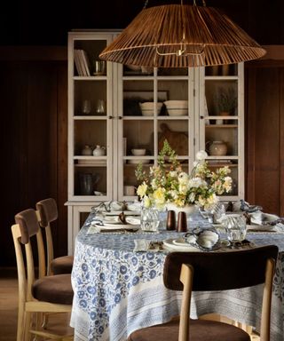 A wooden dining table decorated with a blue and white tablecloth, white china, and a floral centerpiece