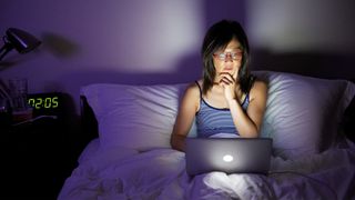 Woman awake at night on her laptop, clock shows it&#039;s 2am