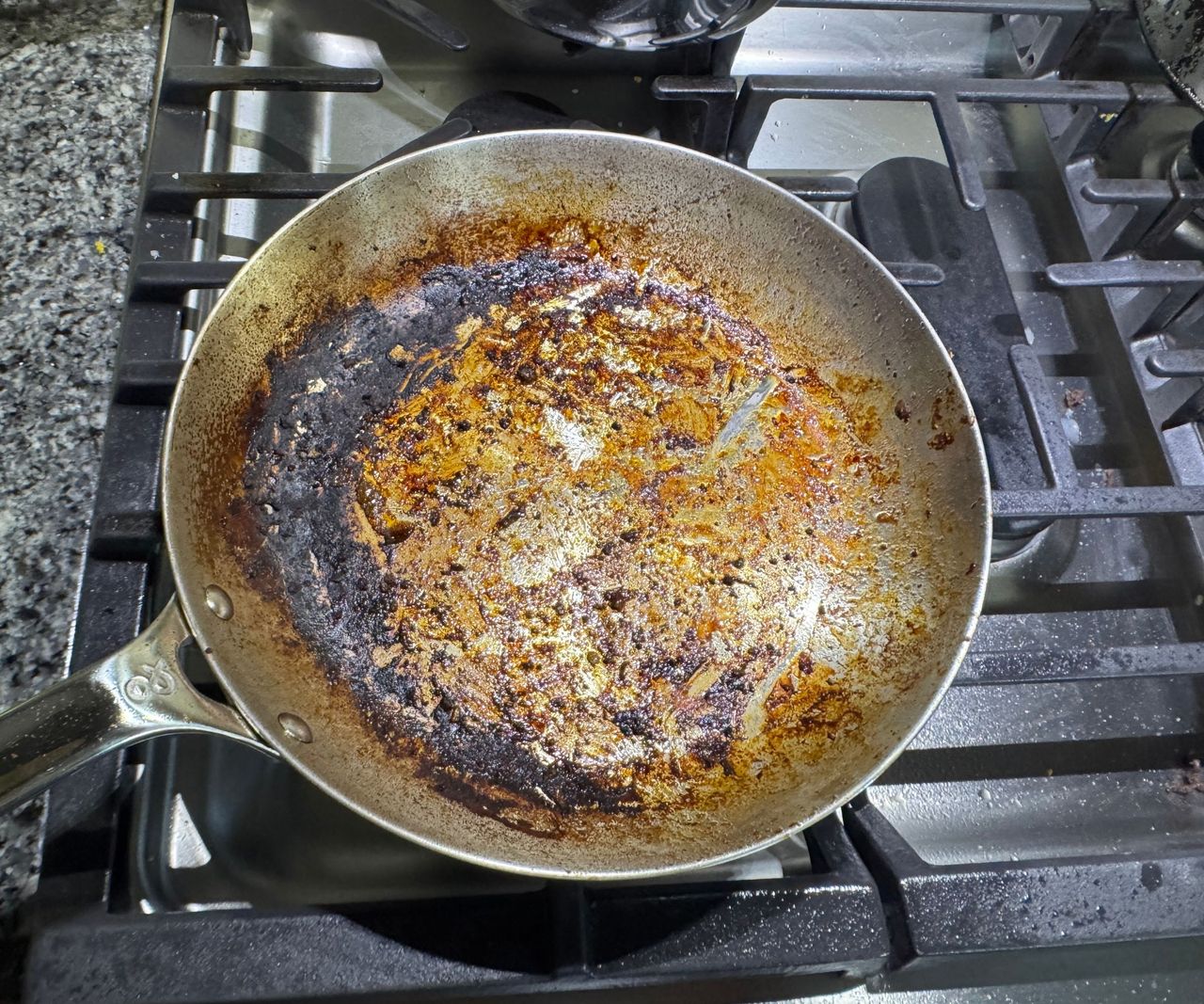 A stainless steel frying pan on a gas stove, with a burnt base