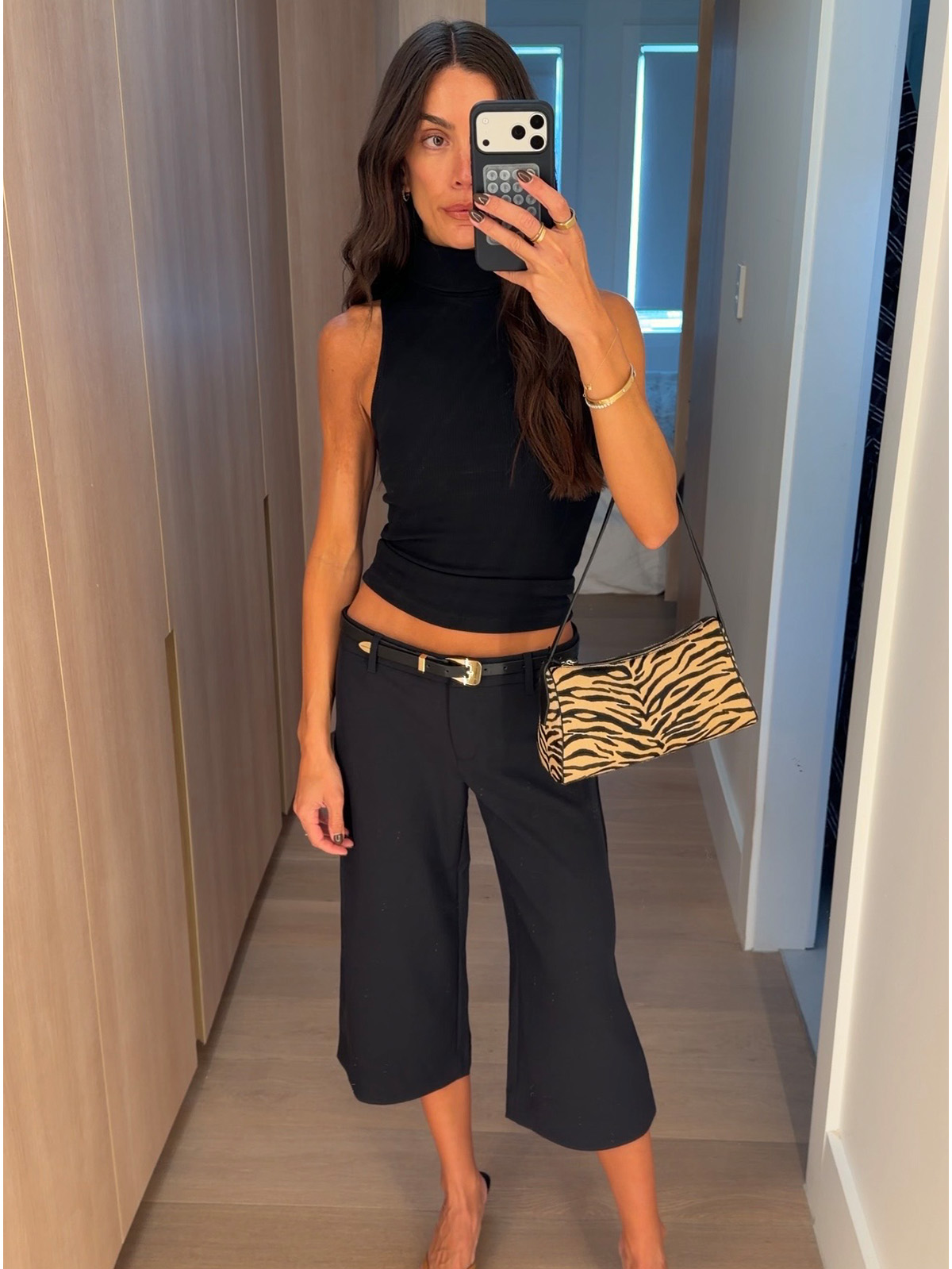Bianca wears a black top, belt, and low-rise capri pants.
