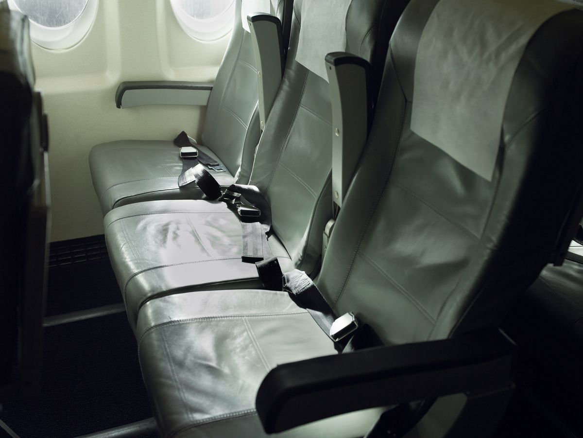 A row of three empty economy seats on an airplane. The middle armrests are raised.