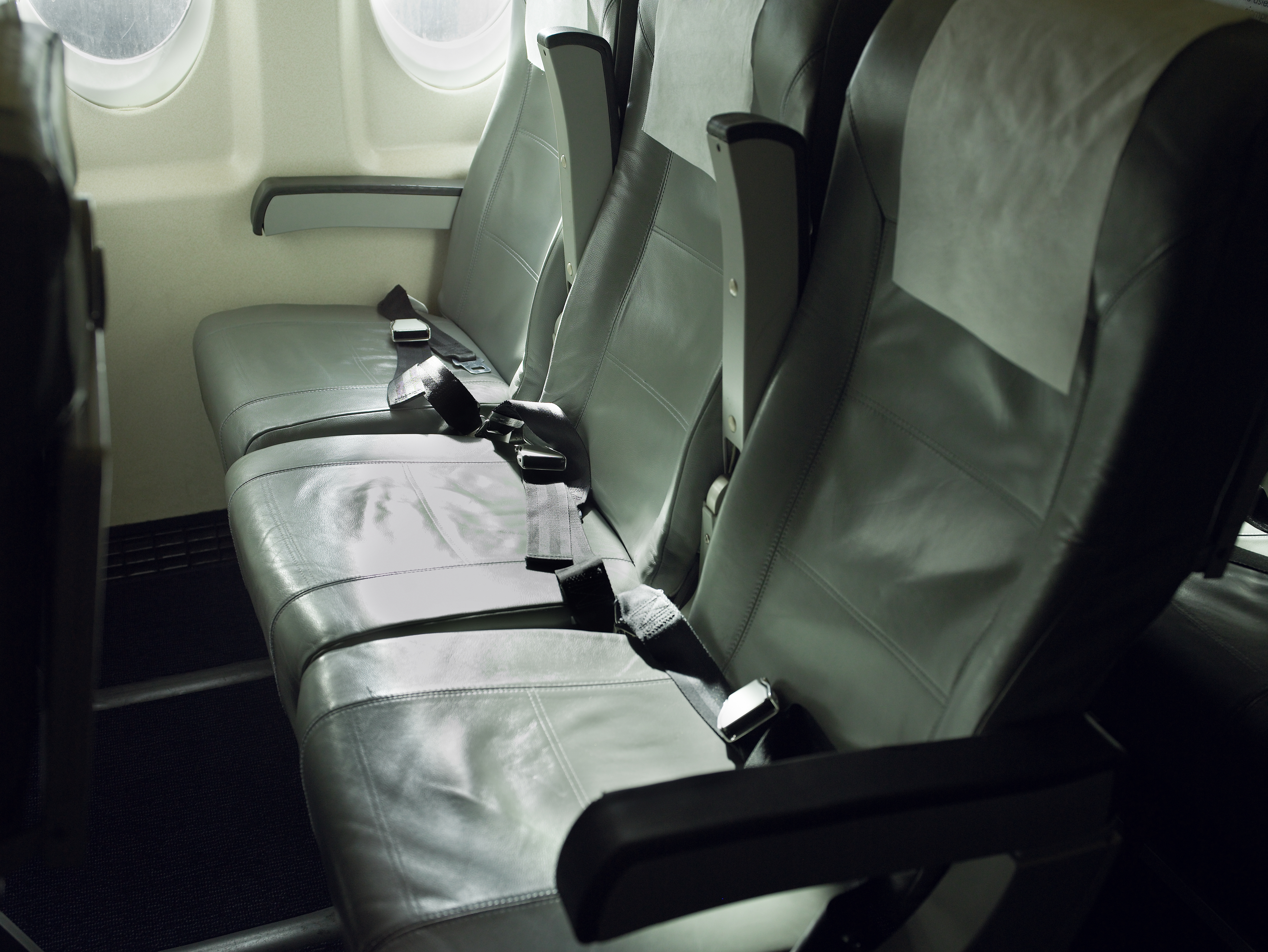 A row of three empty economy seats on an airplane. The middle armrests are raised.