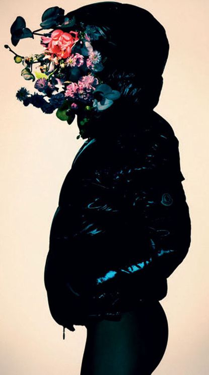 The side view of a woman wearing tight pants, a shiny jacket and a flower decoration covering her face.