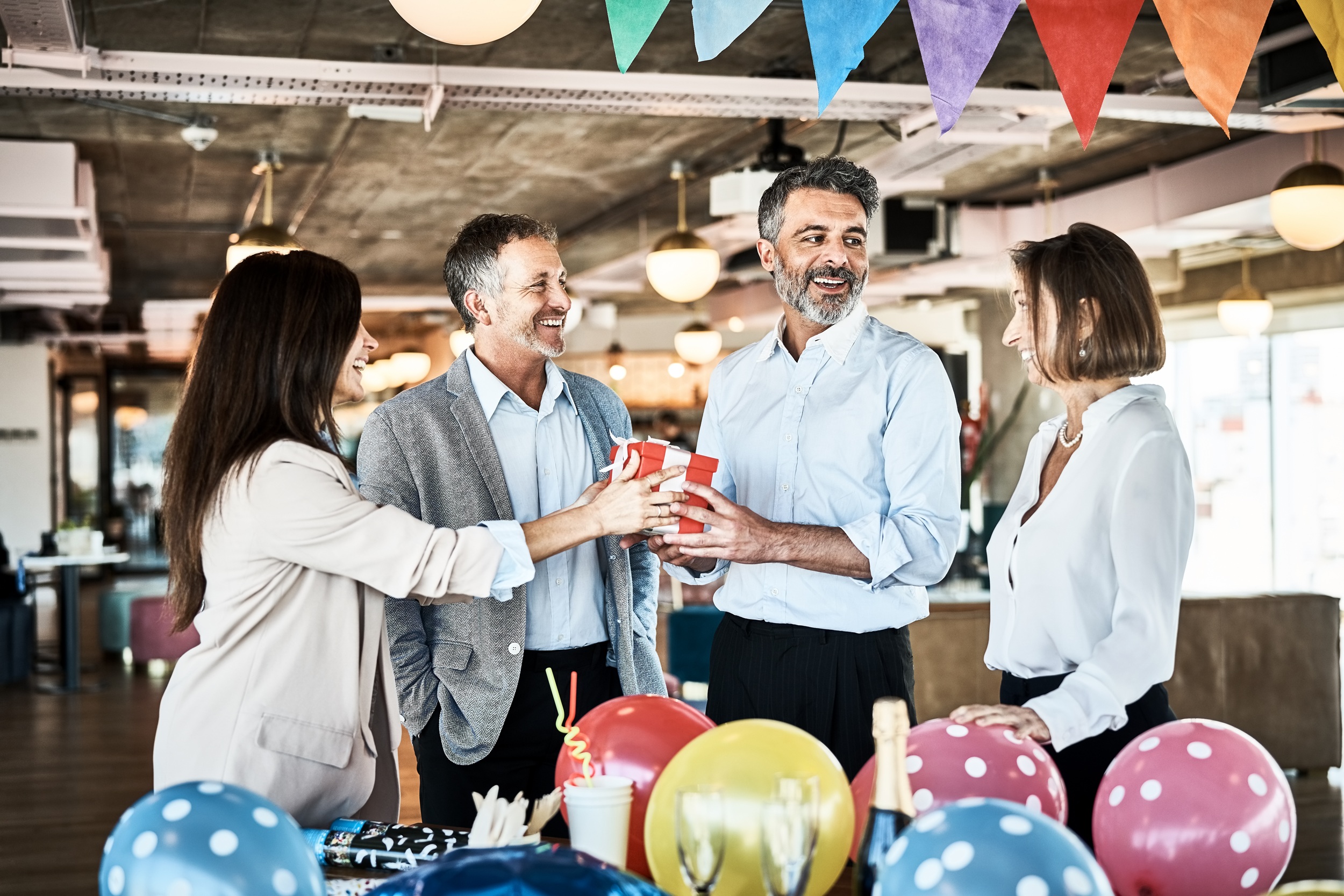 Business people giving birthday present to coworker in office. Business professionals celebrating colleagues birthday in modern office.
