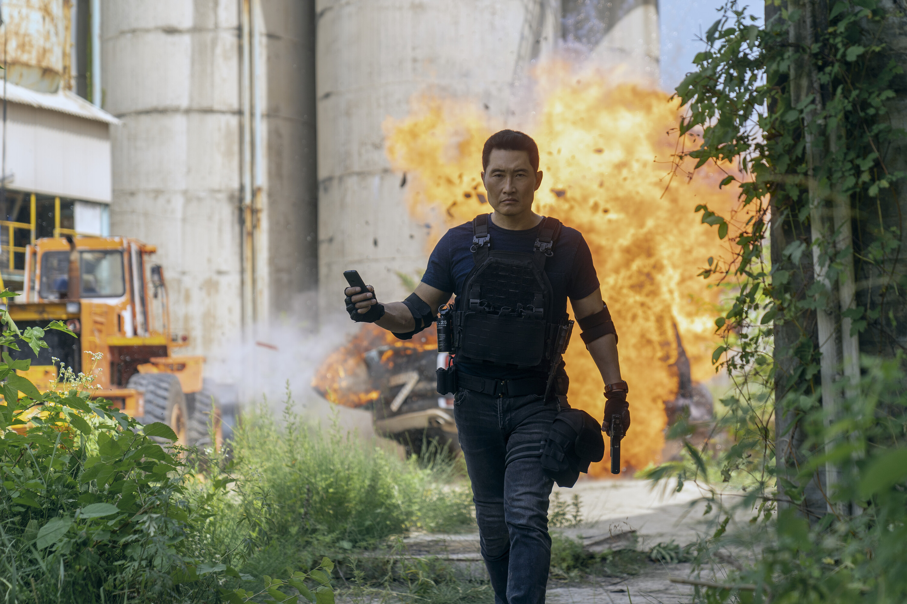 A man (Daniel Dae Kim as David Jung) walks away from an outdoor explosion while holding a detonator, in 'Butterfly' on Prime Video.