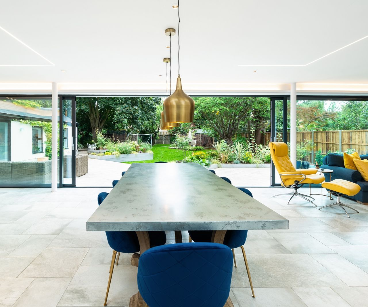 Large open-plan extension with eight-seater grey dining table and blues chairs in front of a large expanse of glazing, Kloeber's KustomFold Mono sliding door