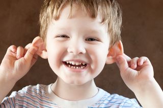 A smiling little boy pulls on his ears.