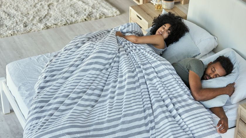A woman looking over at her husband who is fast asleep in shock at how quickly he has fallen asleep, under a striped blanket