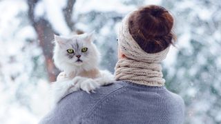 Cat being held by owner outside and looking over her shoulder at camera while the snow falls around them