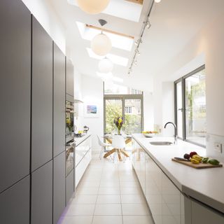 a stylish modern kitchen galley extension, with one tall grey unit, and white counters and cabinets, with doors to the garden, and a vaulted ceiling to add value
