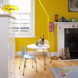Yellow kids room with table and chairs and fireplace