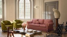 Sunlit living room with wooden floors and arched windows featuring two green accent chair alongside a tonal pink-striped, slipcovered IKEA sofa