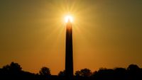 The sun is photographed shining behind the Washington Monument at sunset.
