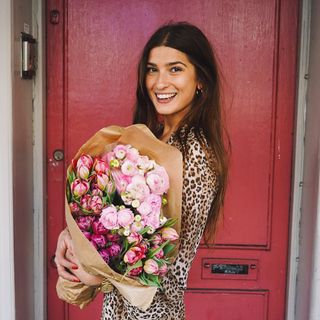 woman with flowers in front of a red door