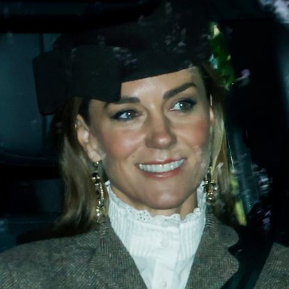 Princess Kate sitting in a car wearing a white blouse and brown hat