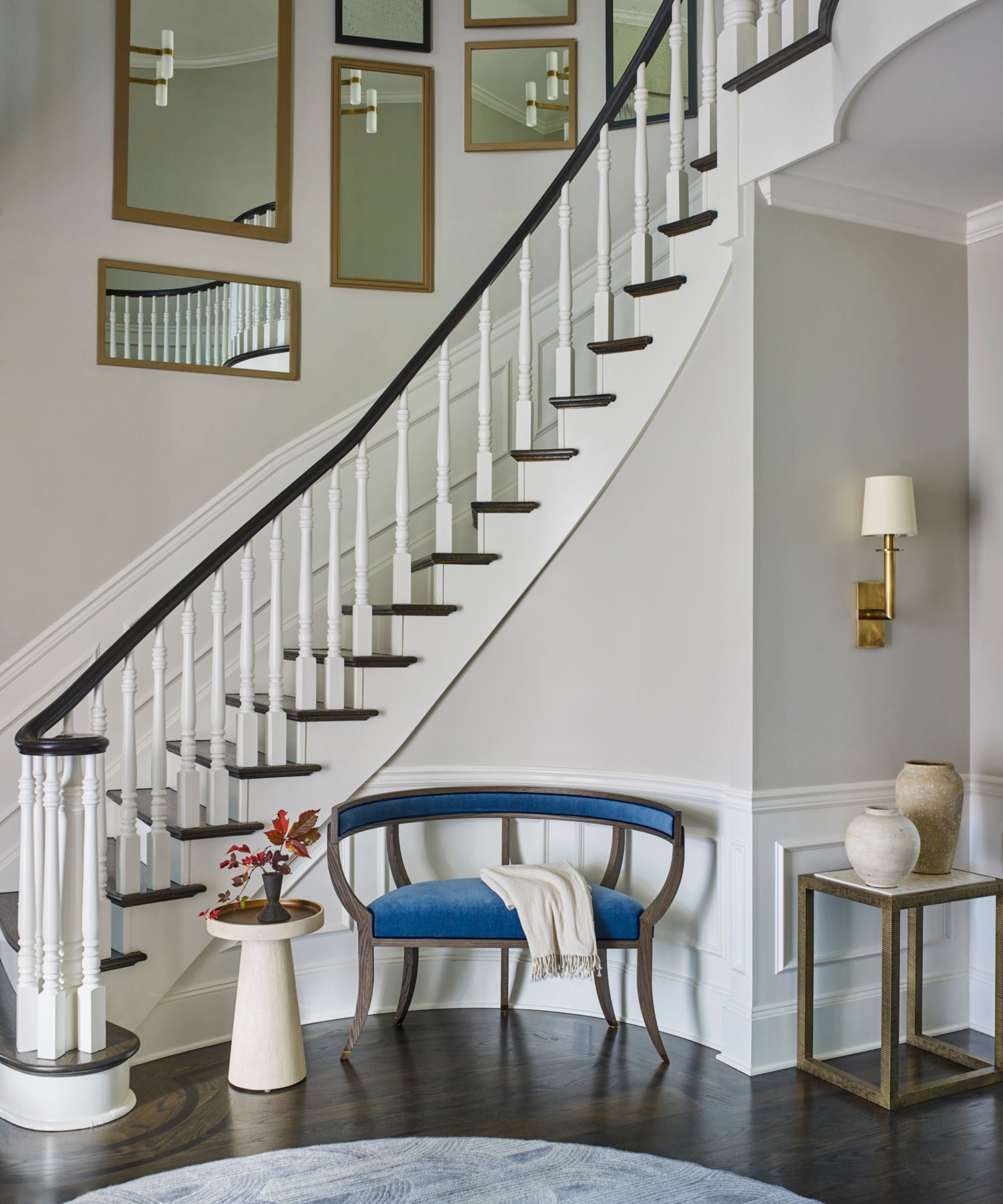 Entryway with dark wood floor, white painted spiral staircase, mirrored wall and velvet blue bench