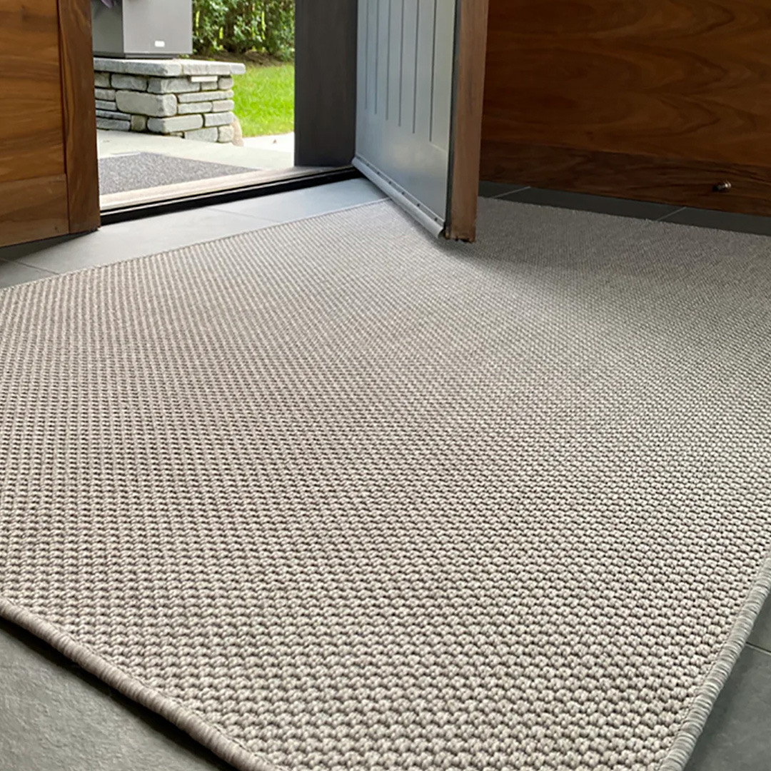 Woven large neutral gray rug shown inside a hallway with door opening to outside 