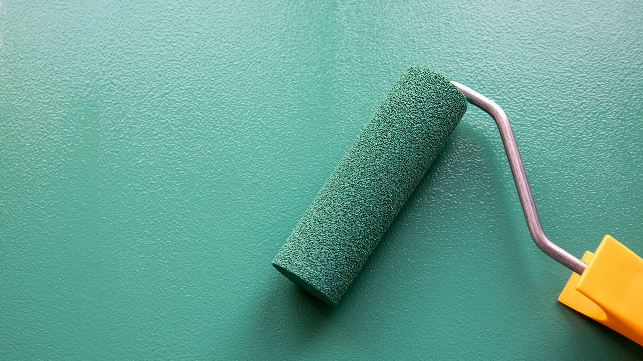 Paint roller with green colour on painted wooden surface