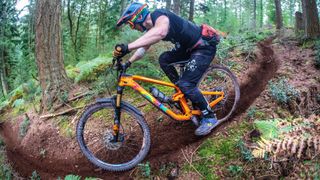 A rider carves a long loamy singletrack corner in some woods