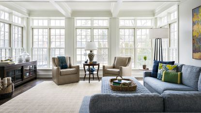 A family room with floor-to-ceiling windows, taupe armchairs and a blue corner sofa