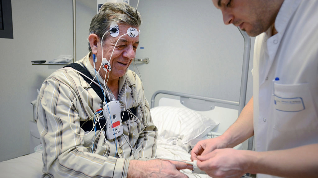 An elderly man linked up to polysomnography as part of a sleep study being helped by a doctor