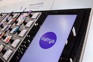 In-store image of the phones section at Currys with various mobiles attached to the wall next to a large TV screen with the Curry logo on it