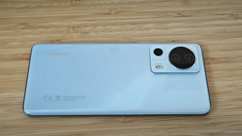 A light-blue Xiaomi 13 Lite camera phone sitting on a wooden desk