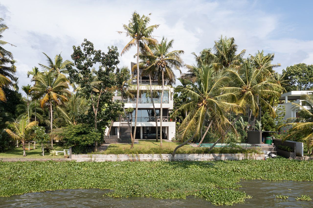 The Plumeria a concrete indian house designed as stacked boxes peaking behind palm trees and tropical planting across a lake