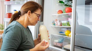 Woman smellling milk from refrigerator