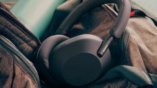 A pair of black Sony WH-1000XM5 headphones on top of a jacket with a water bottle in the top left-hand corner