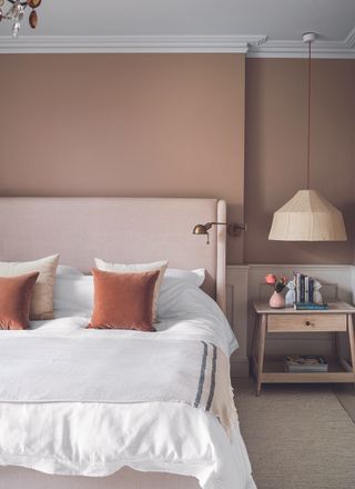 A pink themed bedroom with dusty pink walls, light pink headboard and white sheets