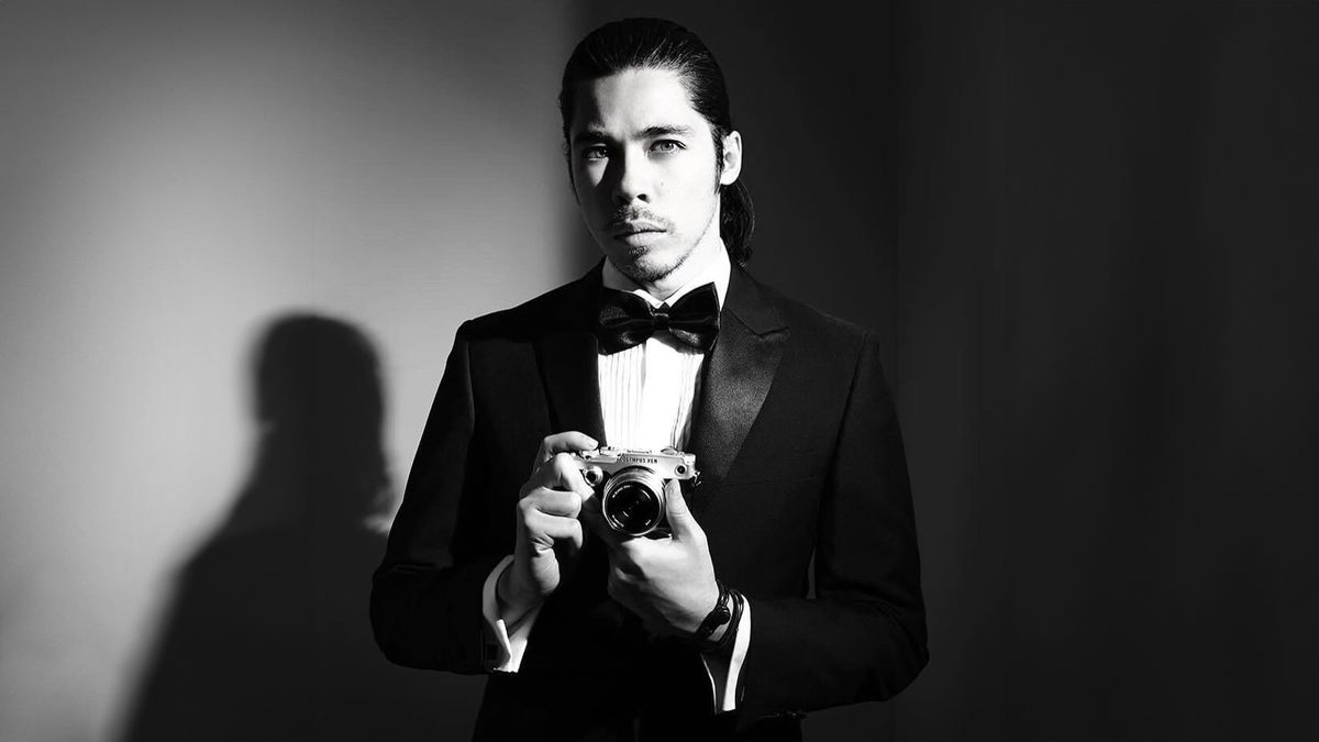 Black-and-white image of a photographer, James Artaius, wearing a tuxedo and holding an Olympus PEN-F camera