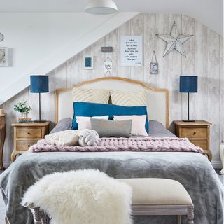 Bed with grey throw in front of a wooden wall