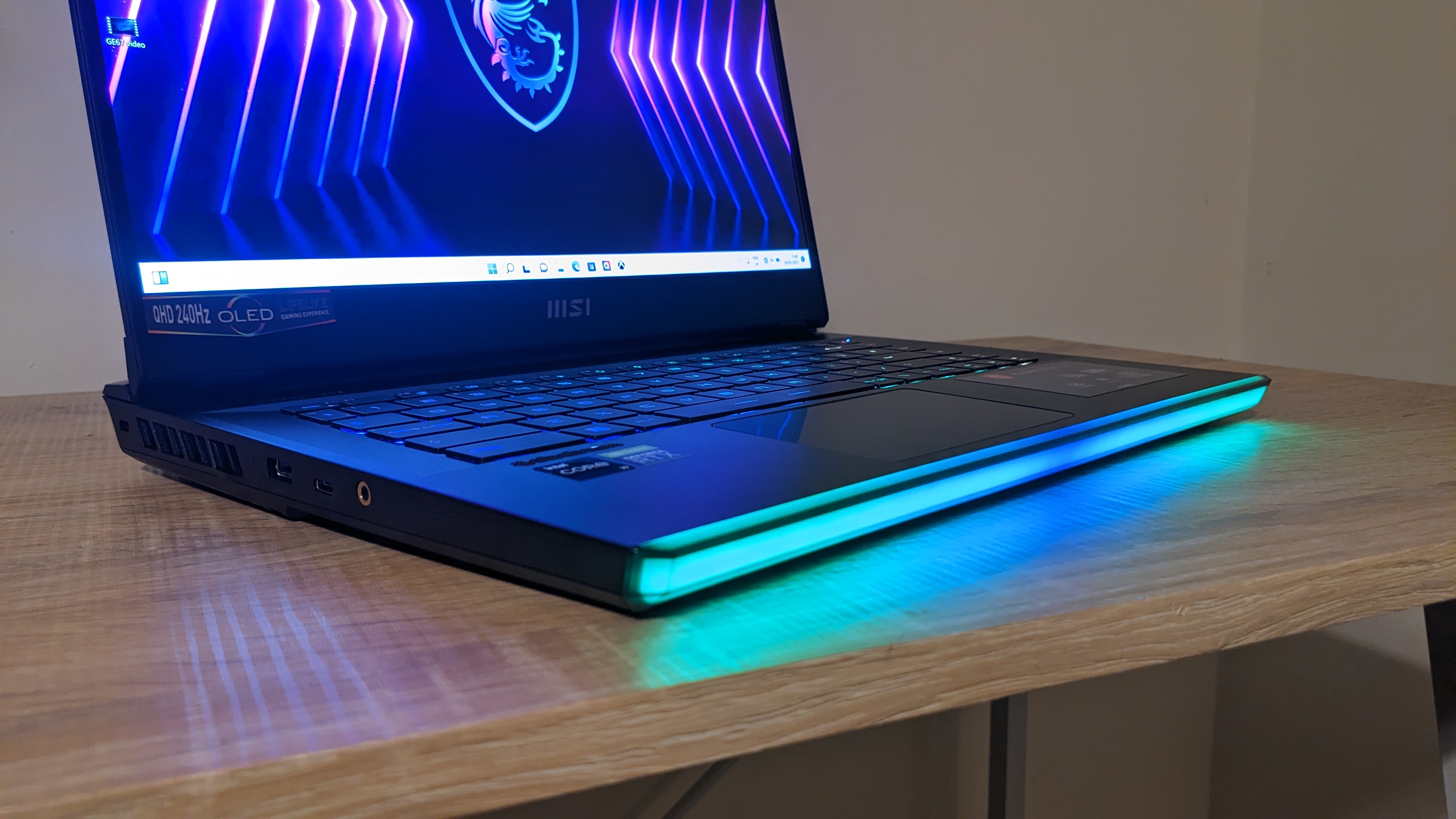 The MSI Raider GE67 HX photographed on a wooden desk with RGB lighting turned on.