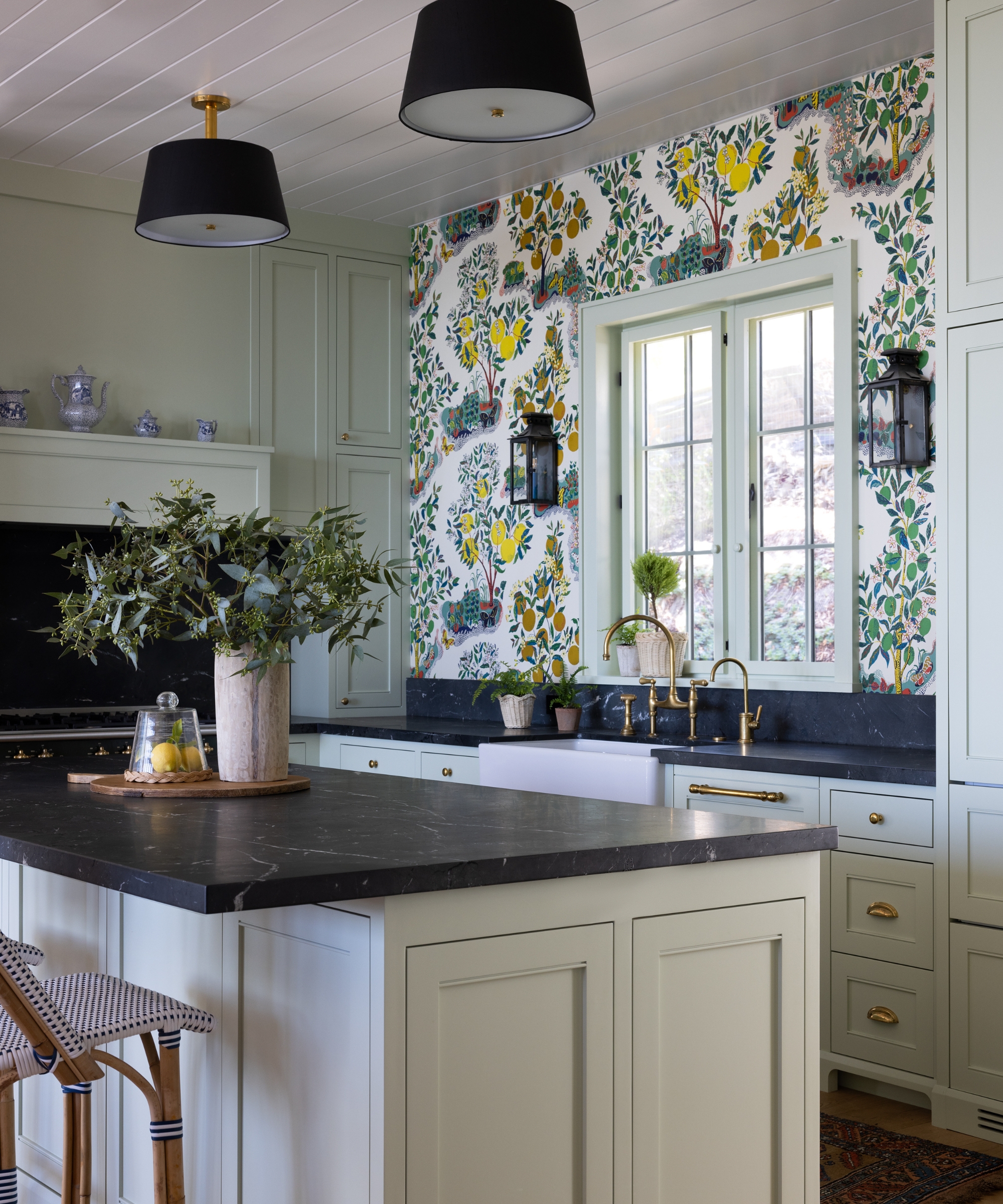 A neutral kitchen with bright wallpaper, black countertops, and an antique cutting board serving as an island tray