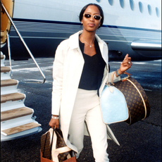 Naomi Campbell wearing a white trench coat and capri trousers. 