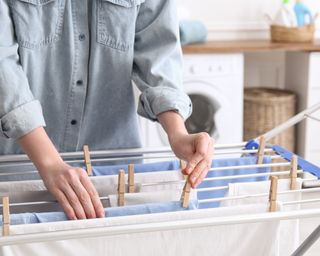 Woman drying clothes with pegs on clothes horse