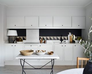 white kitchen with marble topped tables, dark gray splashback, light gray wood floor