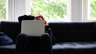 Tired woman sitting on sofa early in the morning, looking at laptop