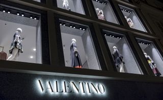 An upward view of the Valentino store with mannequin displays in the windows above the logo.