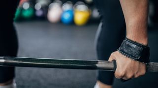 Close up view of woman's hands in lifting straps holding a barbell