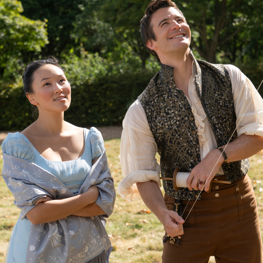 yerin ha as sophie baek wearing a blue dress and luke thompson as benedict bridgerton flying a kite in a sunny field in bridgerton season 4