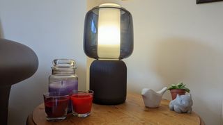 Symfonisk Table Lamp Speaker (Gen 2) on table with candles and a plant - it is turned on