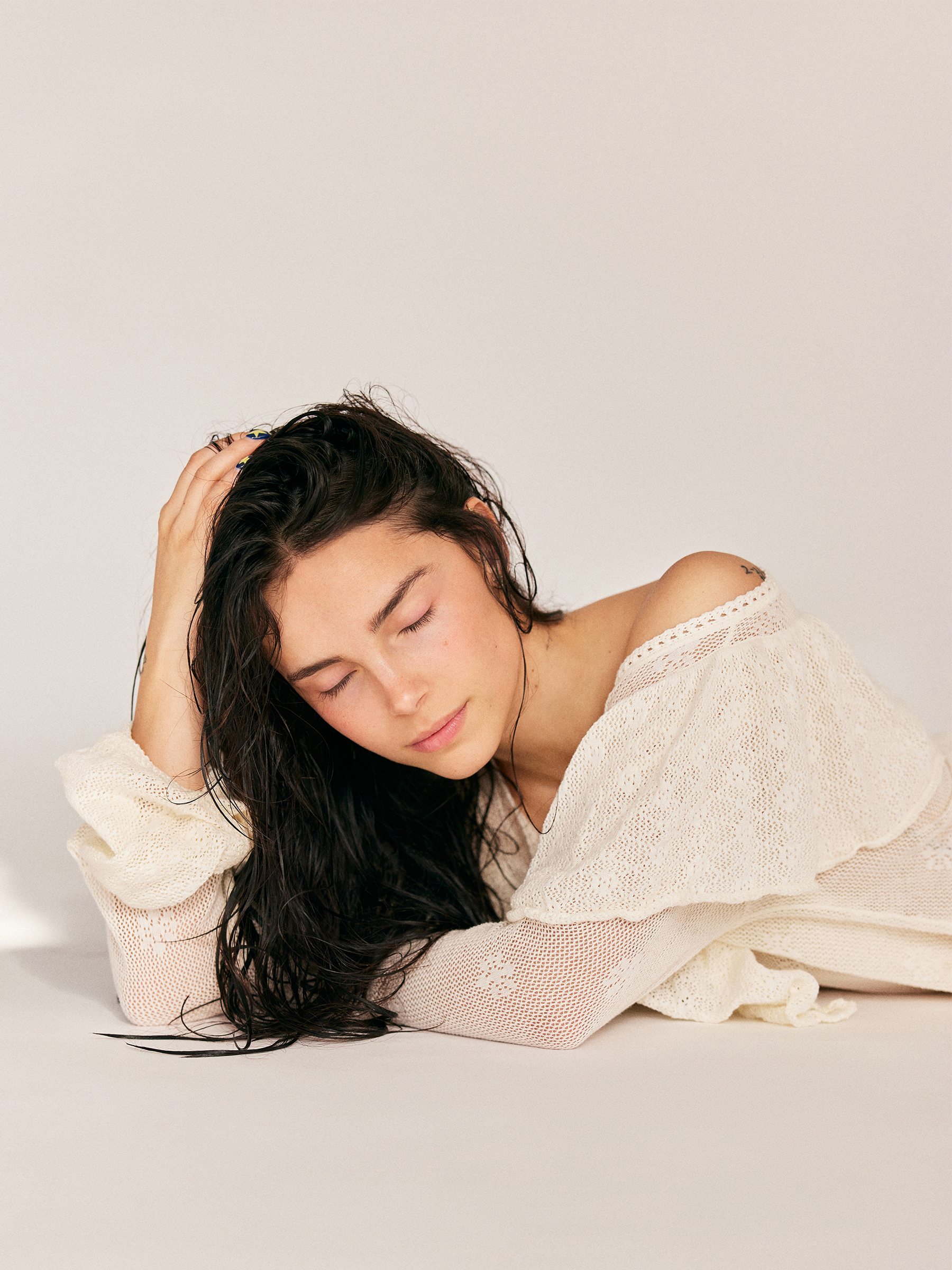 Actress Inde Navarette photographed by Emily Sandifer wearing an off-the-shoulder sheer cream dress. Her hair is wet with pieces falling in front of her face.