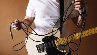 Man wearing a guitar holding a messy guitar cable in his hands