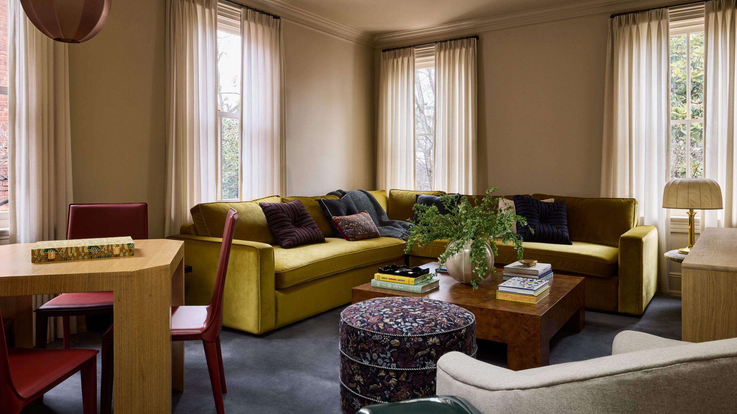 a warm beige family room with full height windows, a chartreuse sectional styled with navy and purple pillows with a burl coffee table, little ottoman and games table with red chairs