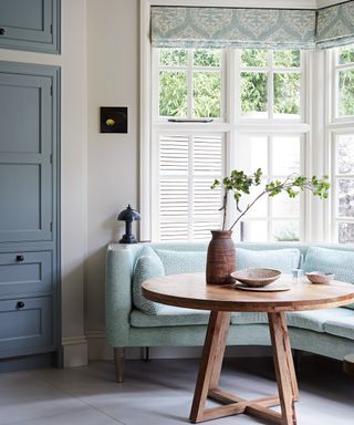 kitchen diner with aqua sofa, aqua patterned cushions, round wooden table and white shutters